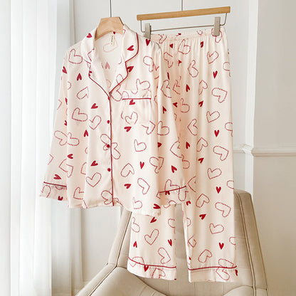 Pigiama donna in raso rosa con cuori rossi, appeso su gruccia. Design elegante e confortevole, ideale per la moda notte femminile.