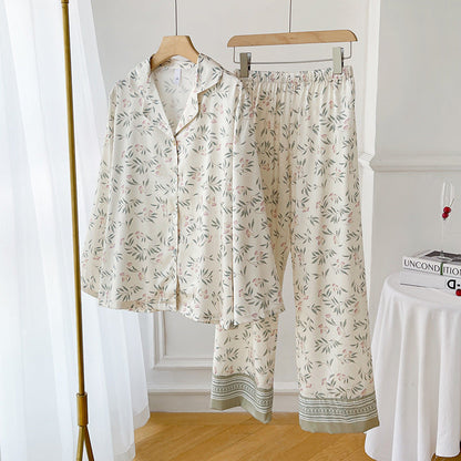 Pigiama donna floreale in raso, camicia e pantaloni, colore bianco con motivi verdi e rosa, appeso su grucce in una stanza luminosa.