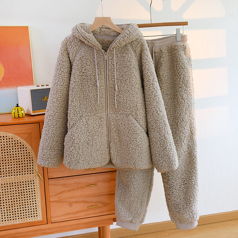 Set pigiama in pile beige, composto da felpa con cappuccio e pantaloni, appeso su gruccia in legno. Arredamento moderno sullo sfondo.