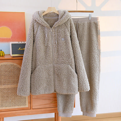 Set pigiama in pile beige, composto da felpa con cappuccio e pantaloni, appeso su gruccia in una stanza luminosa. Abbigliamento comodo e caldo.