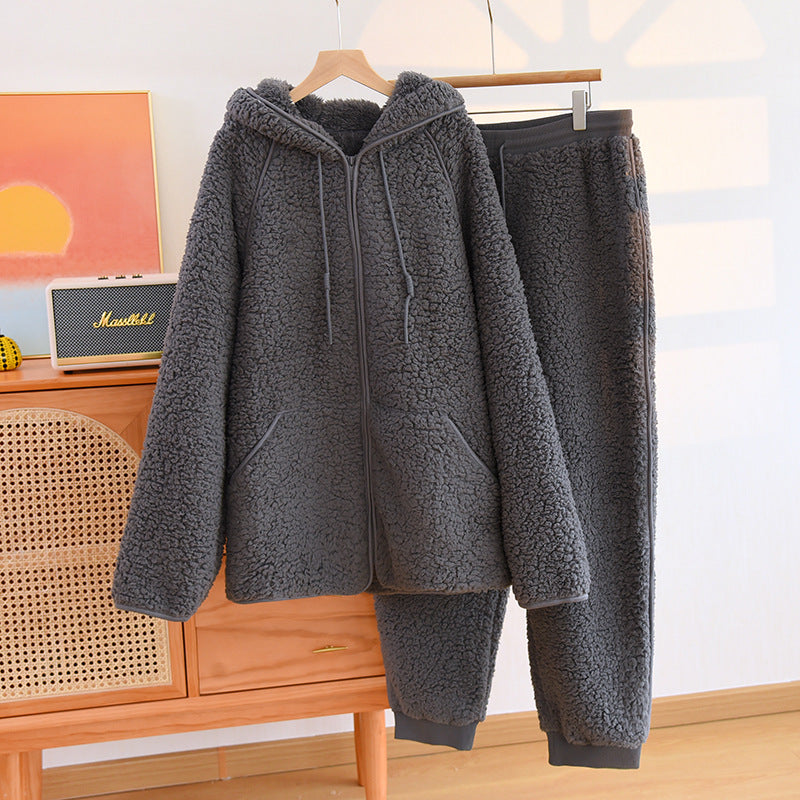 Tuta in pile grigio scuro appesa su gruccia, composta da felpa con cappuccio e pantaloni. Abbigliamento invernale caldo e confortevole.