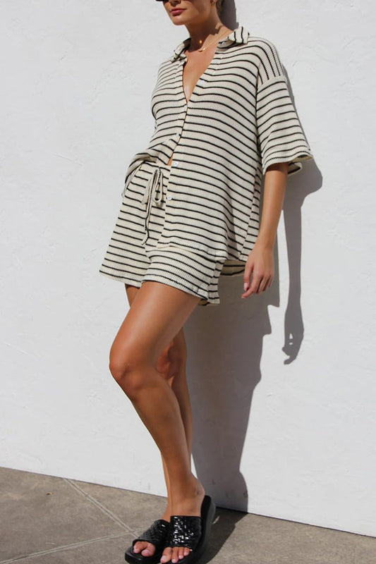 Donna indossa abito estivo a righe bianche e nere, con maniche corte e cintura, sandali neri. Moda casual, look estivo elegante.