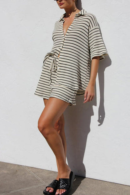 Donna indossa abito estivo a righe bianche e nere, con maniche corte e cintura, sandali neri. Moda casual, look estivo elegante.