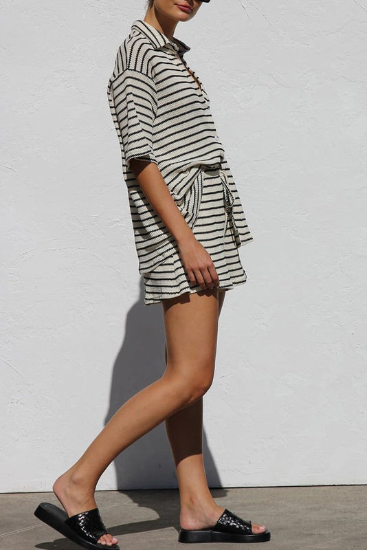 Donna in abito estivo a righe bianche e nere, sandali neri, posa contro un muro bianco. Moda casual, look estivo, abbigliamento femminile.