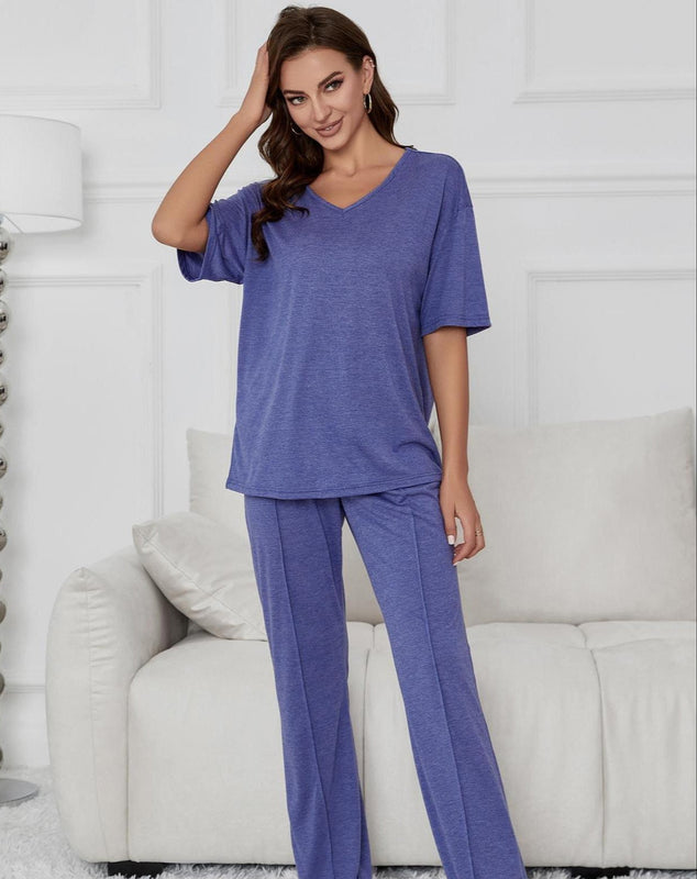 Donna in pigiama blu, posa in salotto moderno con divano bianco e lampada. Abbigliamento comodo, moda casa, stile casual.