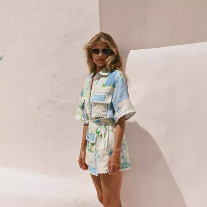 Donna con occhiali da sole indossa un abito estivo a fantasia blu e bianca, sfondo bianco minimalista. Moda estiva, abbigliamento femminile elegante.