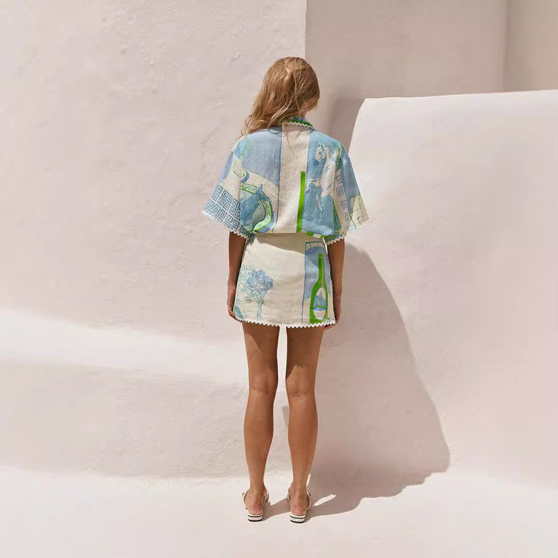 Donna in abito estivo colorato, con motivi geometrici, in piedi contro un muro bianco. Moda estiva, abbigliamento leggero, stile casual.