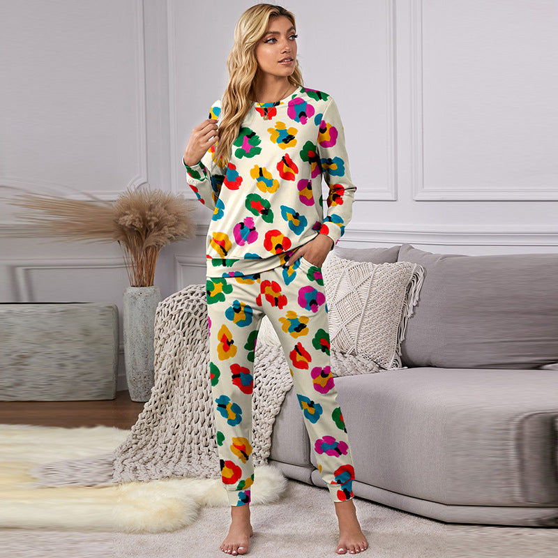 Donna in pigiama colorato floreale, seduta su divano grigio in salotto moderno. Arredamento elegante con tappeto morbido e piante decorative.