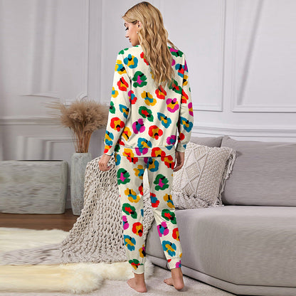 Donna in pigiama colorato con motivi floreali, in piedi in un salotto moderno con divano grigio e decorazioni neutre. Moda pigiama donna.