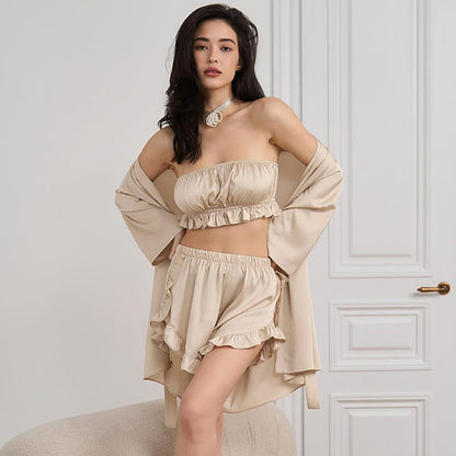Donna in abbigliamento loungewear beige, composto da top senza spalline e shorts con volant, in un ambiente elegante con porta bianca.