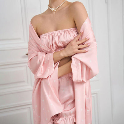 Donna in abbigliamento da notte rosa, con spalle scoperte e collana di perle, in una stanza bianca. Stile elegante e raffinato.
