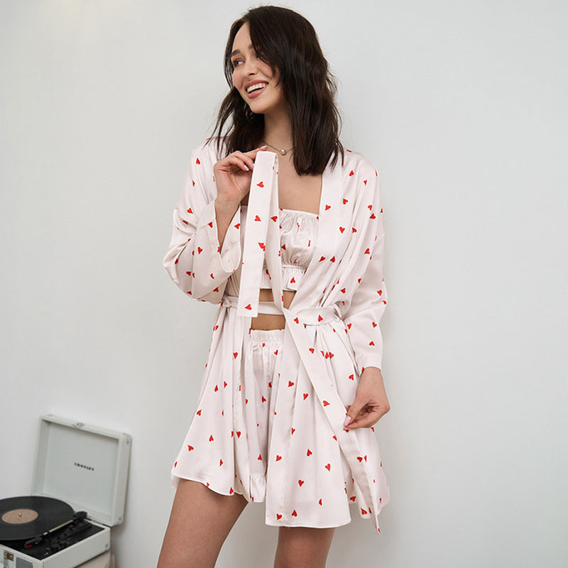 Donna sorridente in pigiama di seta bianco con cuori rossi, accanto a un giradischi vintage. Moda notte elegante e confortevole.