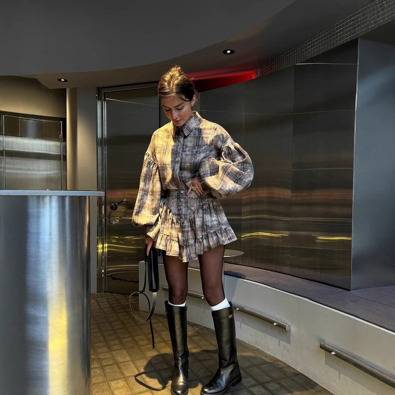 Donna in abito a quadri con stivali neri in un ambiente moderno. Moda autunnale, look elegante, interni contemporanei.