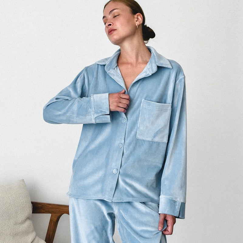 Donna in pigiama di velluto azzurro, elegante e confortevole, posa rilassata in ambiente minimalista. Moda notte, abbigliamento da casa.