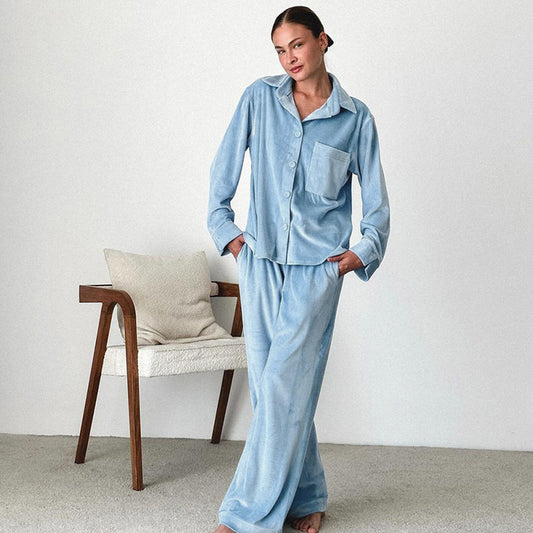 Donna in pigiama azzurro in tessuto morbido, posa accanto a sedia moderna con cuscino bianco. Stile casual, comfort, moda casa.