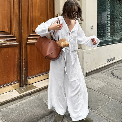 Donna in abito bianco lungo con borsa marrone e baguette, cammina su marciapiede cittadino. Moda urbana, stile casual chic, shopping.