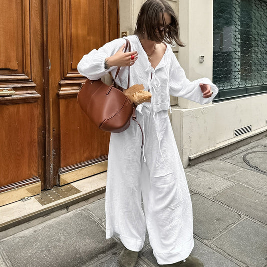 Donna in abito bianco lungo con borsa marrone e baguette, cammina su marciapiede cittadino. Moda urbana, stile casual chic, shopping.