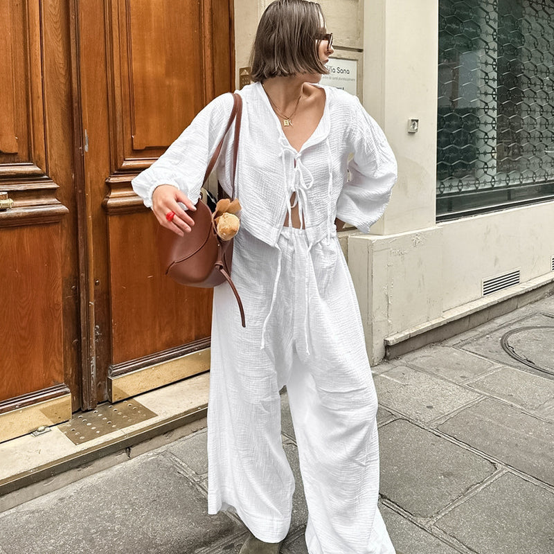 Donna con abito bianco estivo, borsa marrone e peluche, cammina su marciapiede cittadino. Moda urbana, stile casual chic, estate.