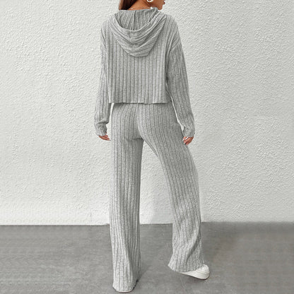 Donna in tuta grigia a coste, con cappuccio e pantaloni larghi, vista posteriore. Moda casual, abbigliamento comodo, stile autunnale.