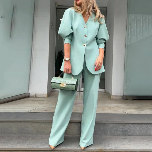 Donna in elegante tailleur verde menta con giacca a bottoni e pantaloni larghi, borsa coordinata, scarpe a punta. Moda femminile chic e moderna.