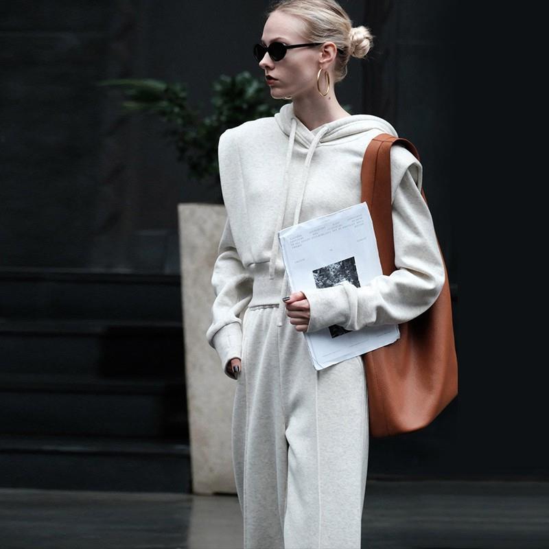 Donna con occhiali da sole indossa tuta sportiva grigia e borsa marrone, tiene documenti. Moda urbana, stile casual chic, tendenze autunno.