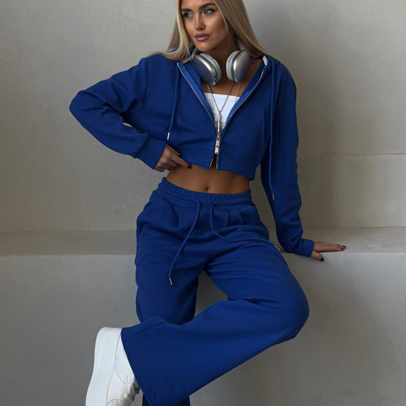 Donna in tuta sportiva blu con cuffie, top bianco e scarpe da ginnastica bianche. Moda casual, abbigliamento comodo, stile urbano.