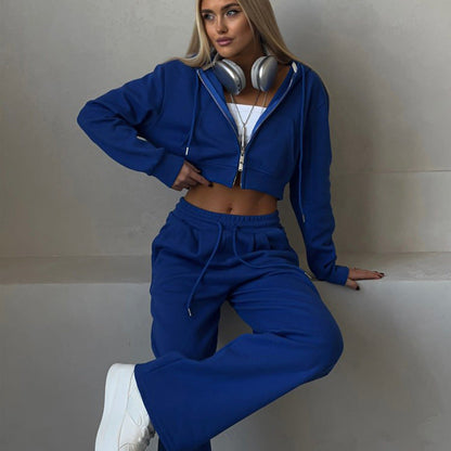 Donna in tuta sportiva blu con cuffie, top bianco e scarpe da ginnastica bianche. Moda casual, abbigliamento comodo, stile urbano.