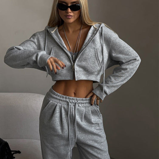 Donna in tuta grigia sportiva, occhiali da sole neri, posa moderna. Abbigliamento casual, moda streetwear, stile urbano.