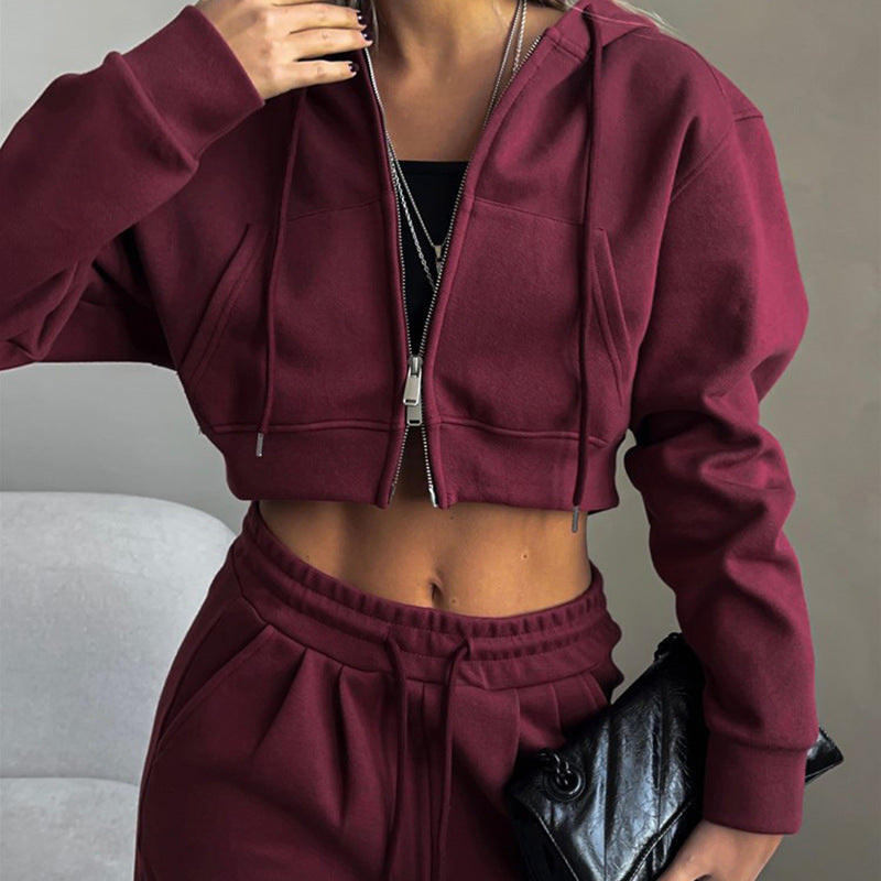Donna in tuta sportiva bordeaux, felpa con cappuccio e pantaloni, tiene una borsa nera. Abbigliamento casual moda autunno inverno.
