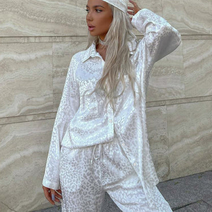 Donna con pigiama di seta bianco leopardato, posa elegante contro parete di marmo. Moda femminile, abbigliamento notte, stile lussuoso.