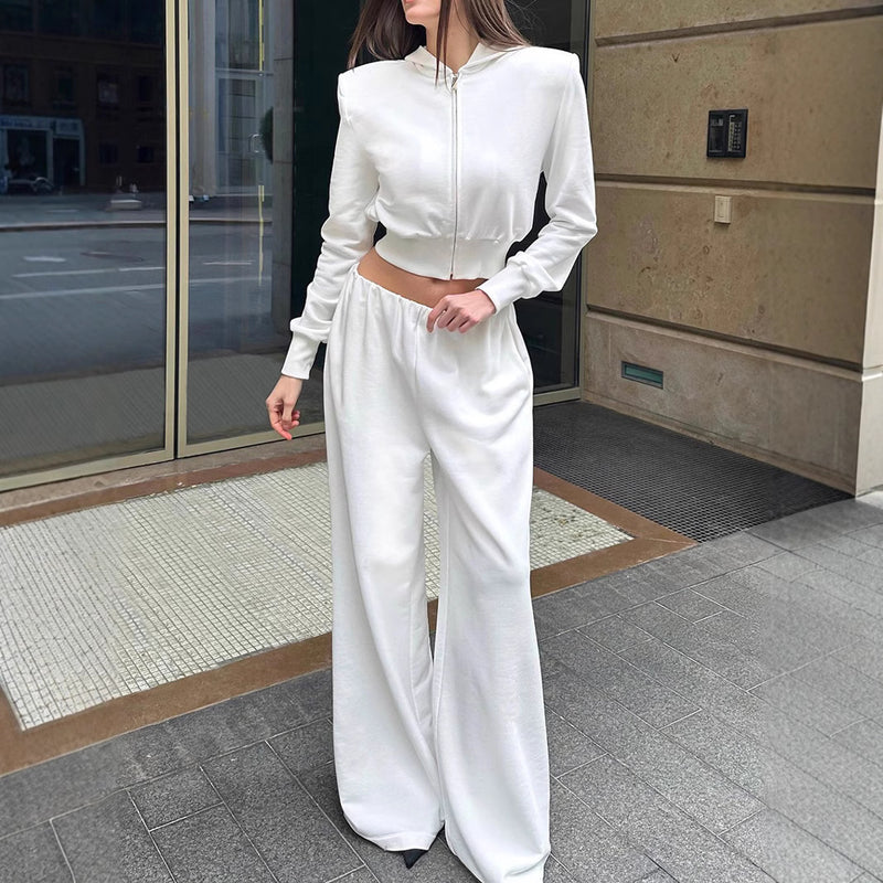 Donna in tuta bianca elegante, con giacca corta e pantaloni larghi, posa davanti a un edificio moderno. Moda casual chic, abbigliamento urbano.
