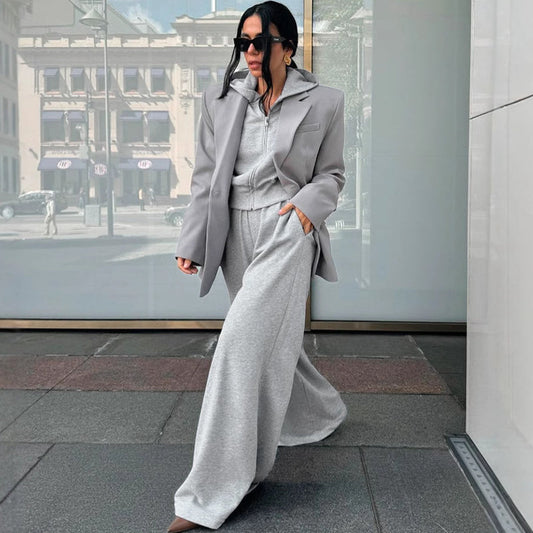 Donna con occhiali da sole indossa completo grigio elegante, giacca oversize e pantaloni larghi, cammina in città moderna. Moda urbana autunnale.