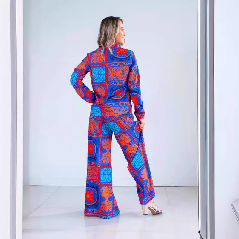 Donna in tuta colorata blu e arancione con motivi geometrici, posa di spalle in un corridoio moderno. Moda femminile, abbigliamento vivace.
