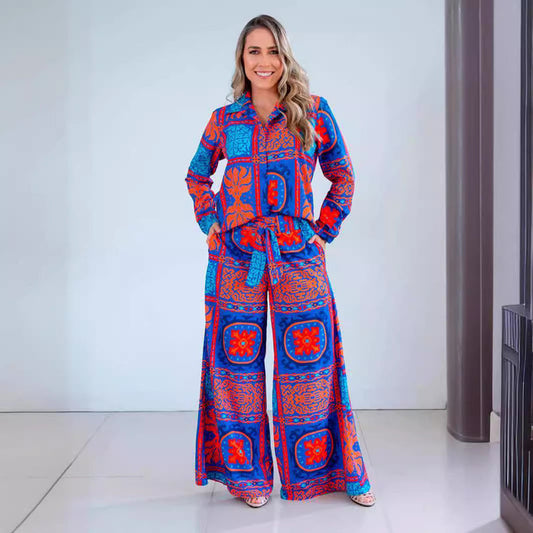 Donna sorridente in tuta colorata blu e rossa con motivi geometrici, posa in un ambiente moderno. Moda femminile, abbigliamento vivace, stile casual.