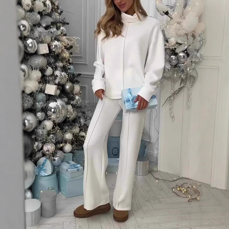 Donna in abbigliamento invernale bianco con pacco regalo blu, accanto ad albero di Natale decorato con ornamenti argentati e bianchi.