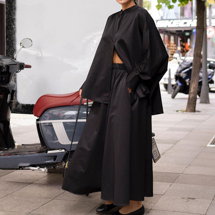 Donna in abito nero oversize su marciapiede urbano, accanto a scooter. Moda street style, abbigliamento casual elegante, tendenze autunno.