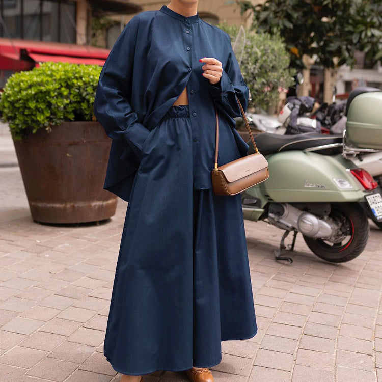 Donna con abito lungo blu scuro e borsa a tracolla marrone, accanto a una Vespa verde su strada cittadina. Moda urbana elegante.