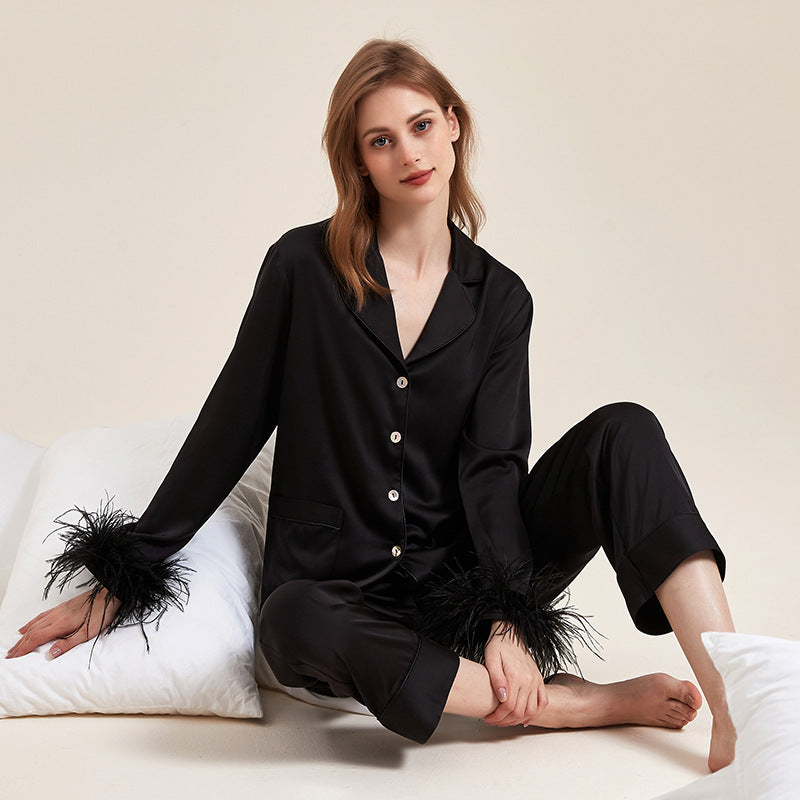 Donna in pigiama di seta nero con piume, seduta su cuscini bianchi. Moda notte elegante, abbigliamento da casa lussuoso, comfort e stile.