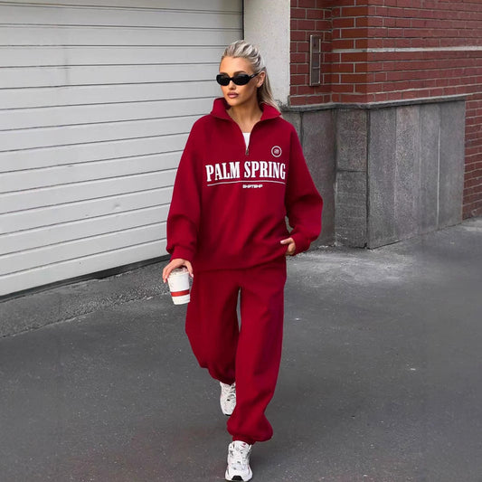 Donna con occhiali da sole indossa tuta rossa "Palm Spring", cammina con caffè in mano. Moda casual, street style, abbigliamento sportivo urbano.