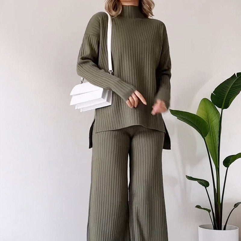 Donna in completo maglia verde oliva, borsa bianca a tracolla, pianta decorativa. Moda autunnale, abbigliamento casual elegante, stile minimalista.