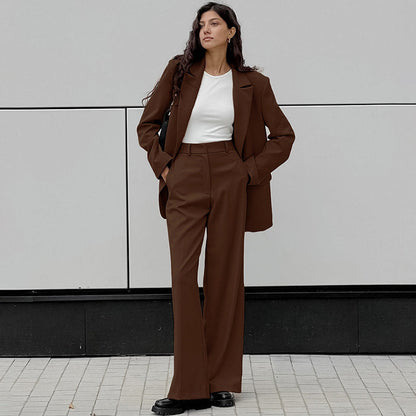 Donna in abito marrone elegante, giacca e pantaloni, su sfondo grigio. Moda autunnale, stile business casual, tendenze abbigliamento femminile.