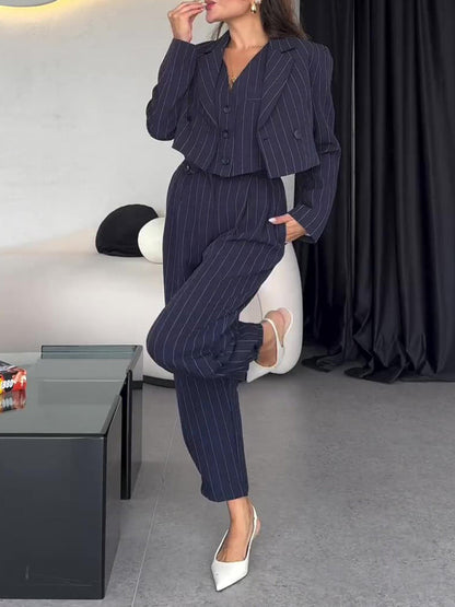 Donna in elegante completo gessato blu scuro, giacca e pantaloni, posa in salotto moderno. Moda femminile, abbigliamento formale, stile contemporaneo.