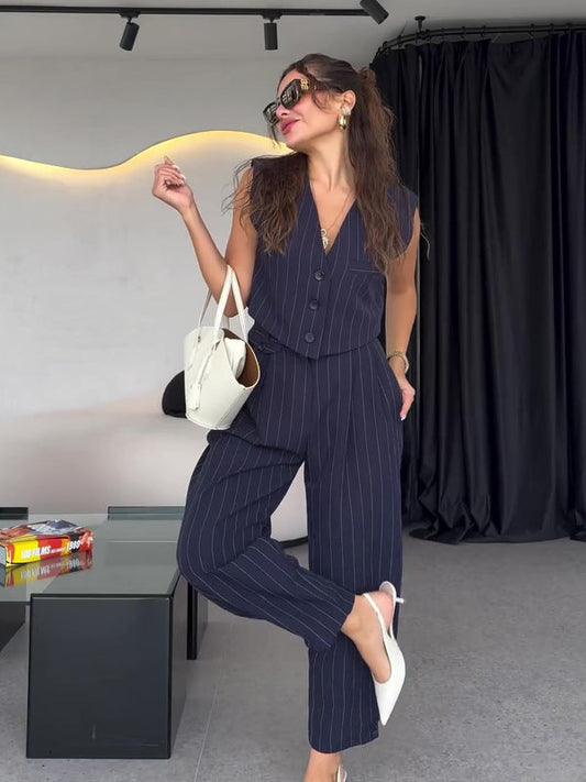 Donna elegante in completo gessato blu scuro, borsa bianca e occhiali da sole, posa in un ambiente moderno. Moda femminile, stile sofisticato.
