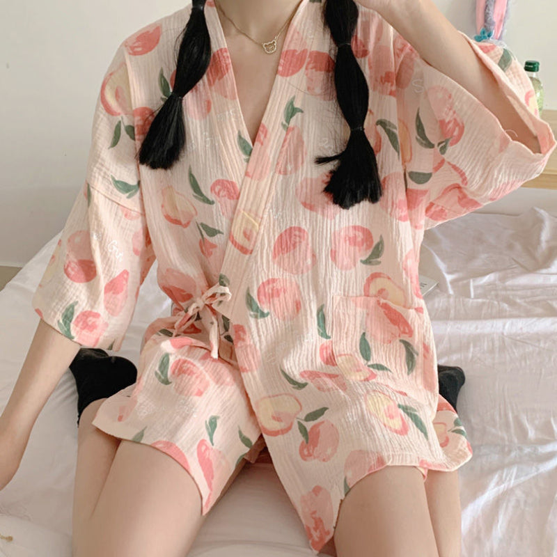Kimono estivo rosa con stampa di pesche, indossato da una persona seduta. Tessuto leggero e morbido, ideale per giornate calde.