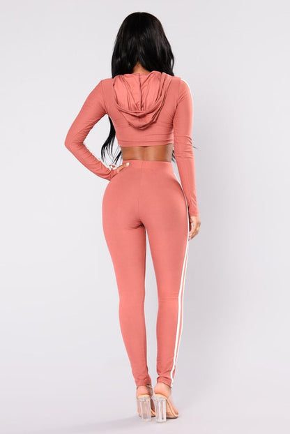 Donna in abbigliamento sportivo rosa, con cappuccio e pantaloni aderenti, vista posteriore. Moda fitness, abbigliamento attivo, stile casual.