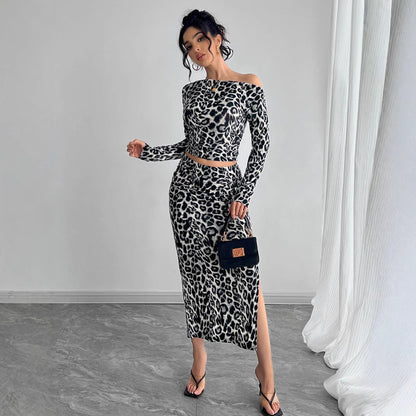 Donna in abito leopardato a spalle scoperte, con borsa nera e sandali, posa in una stanza moderna con tende bianche. Moda femminile elegante.