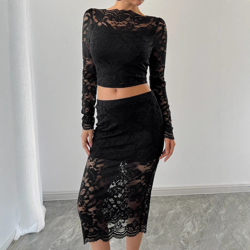 Donna in abito nero in pizzo trasparente, maniche lunghe, gonna midi, posa elegante su sfondo neutro. Moda femminile, abbigliamento chic.