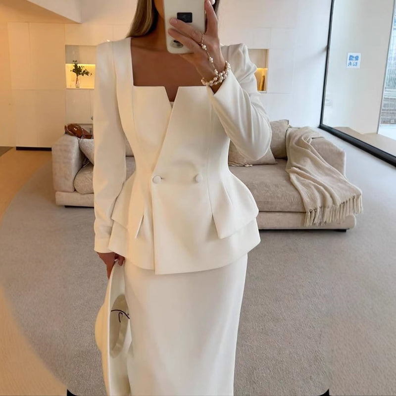 Donna in elegante abito bianco sartoriale, giacca con scollo quadrato e bottoni, in un salotto moderno. Moda femminile, abbigliamento formale.