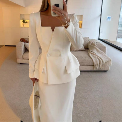 Donna in elegante abito bianco sartoriale, giacca con scollo quadrato e bottoni, in un salotto moderno. Moda femminile, abbigliamento formale.