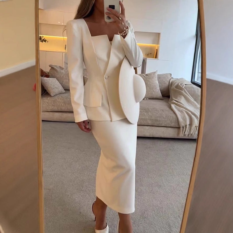 Abito elegante bianco con giacca strutturata e gonna lunga, indossato da una donna davanti a uno specchio. Design moderno e sofisticato.
